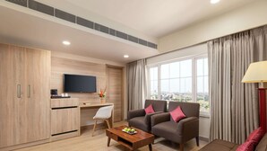 A modern living room with a sofa, armchair, coffee table, TV, and a desk with a chair. - Nidhivan Sarovar Portico Vrindavan (Mathura)