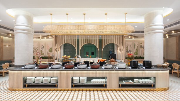 A buffet area with a variety of food items, a central decorative wall, and a patterned floor. - Nidhivan Sarovar Portico Vrindavan (Mathura)
