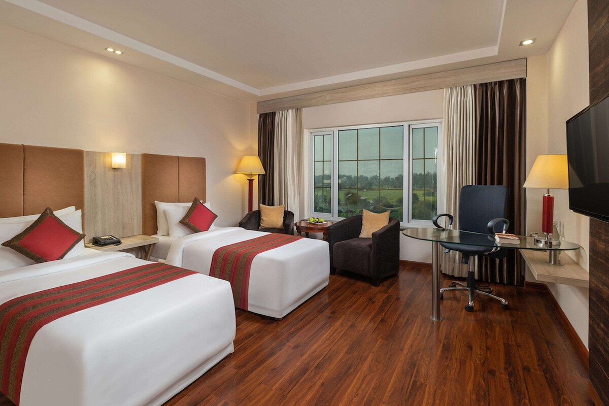 A hotel room with two beds, a desk, a chair, and a TV.
