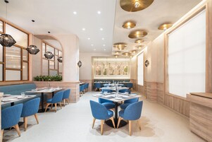 Interior moderno de restaurante con sillas tapizadas en azul, mesas redondas y una combinación de iluminación colgante y empotrada.