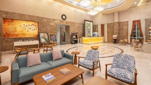A spacious lobby with a reception desk, seating area, and artwork on the walls. - Nidhivan Sarovar Portico Vrindavan (Mathura)