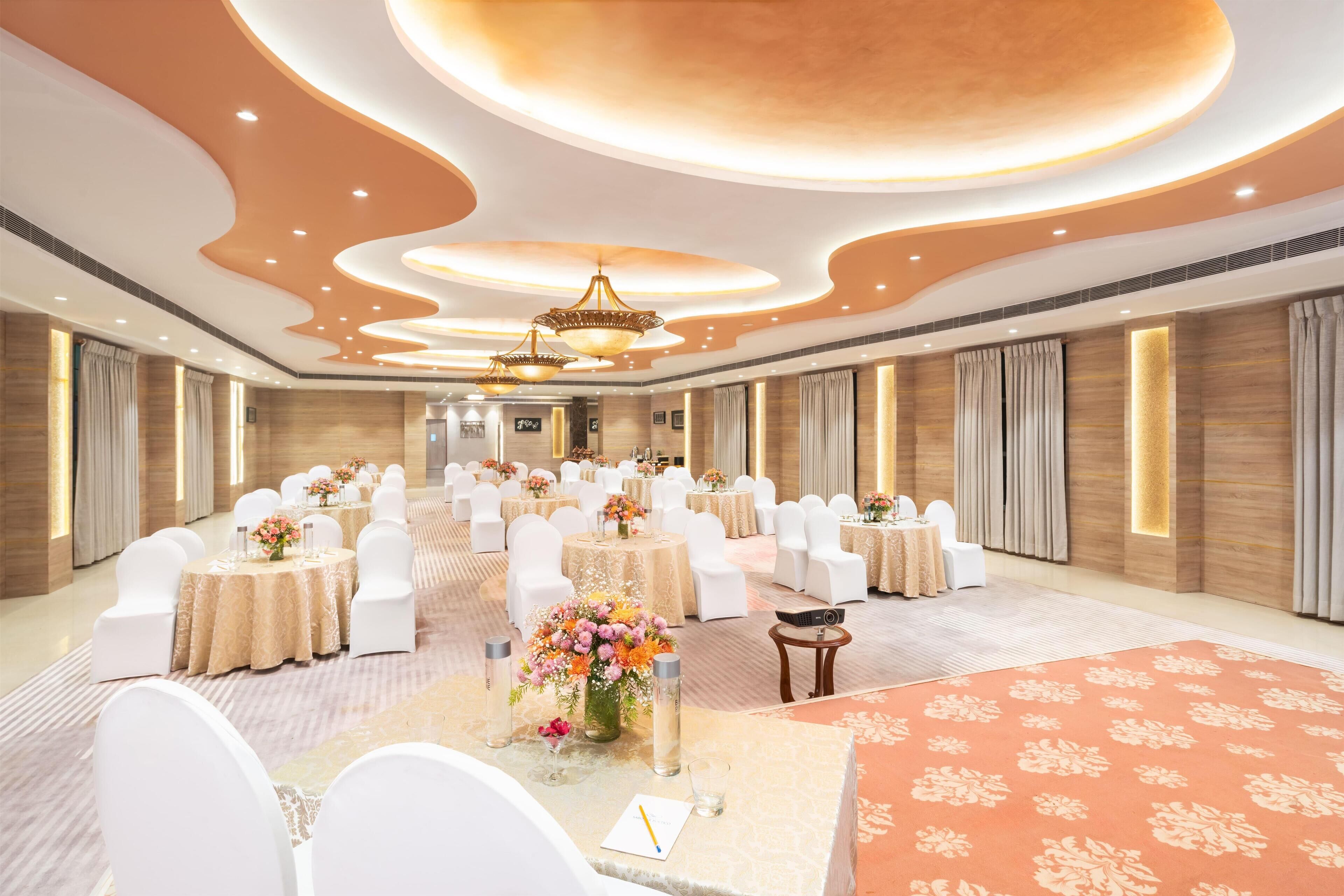A spacious banquet hall with round tables, white chairs, and floral centerpieces.