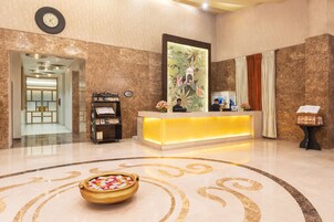 Zona de recepción de hotel con suelo de mármol, mostrador de recepción, un reloj y un elemento decorativo en la pared.