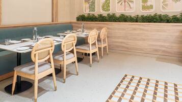A restaurant with a green booth seating area, wooden chairs, and a patterned rug.