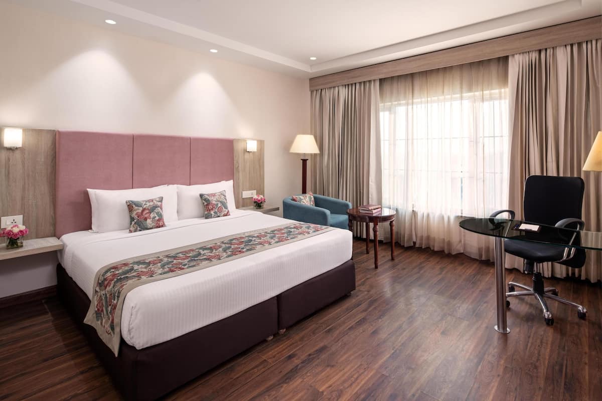 A hotel room with a large bed, a desk, a chair, and a window with curtains.