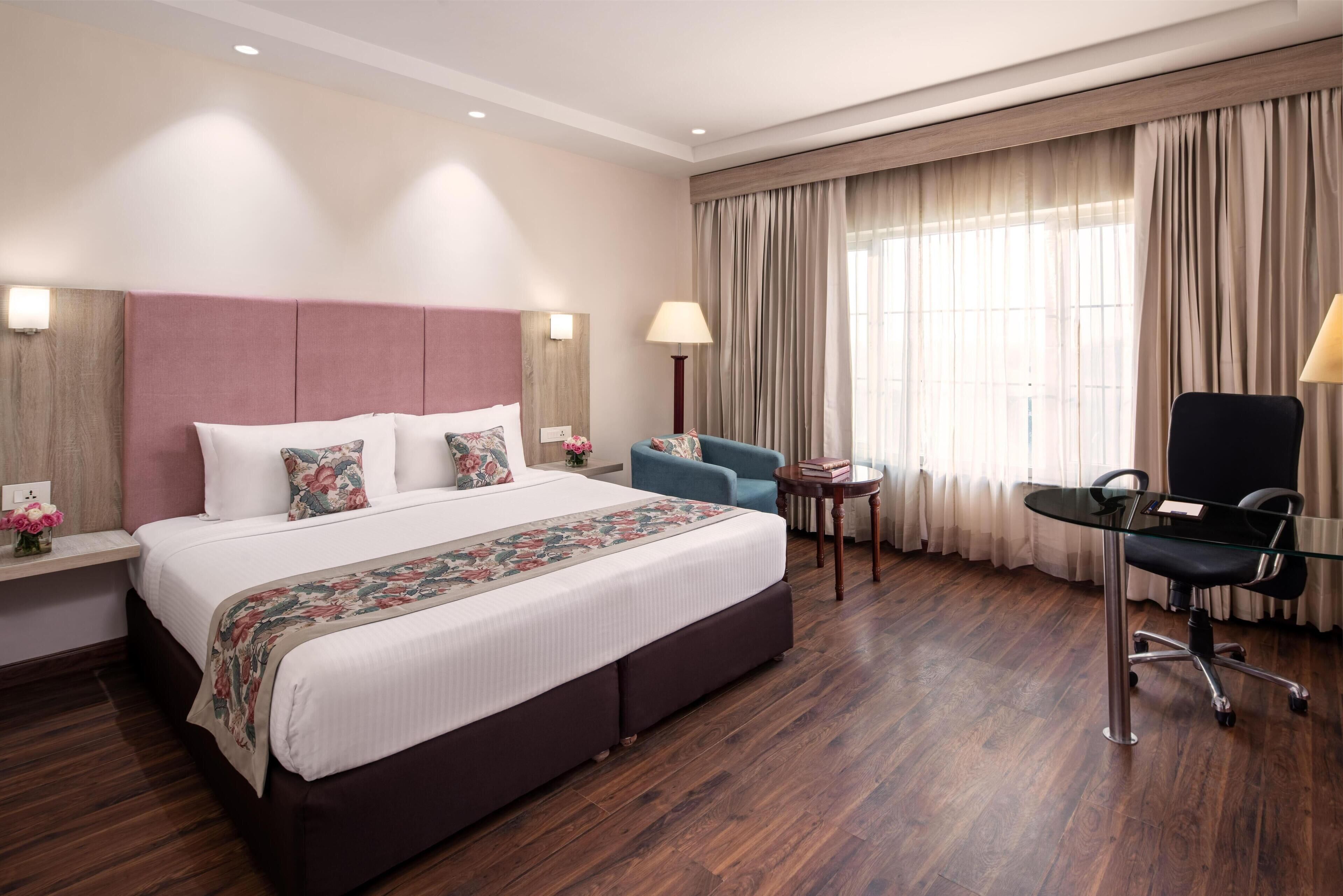 A hotel room with a large bed, a desk, a chair, and a window with curtains.