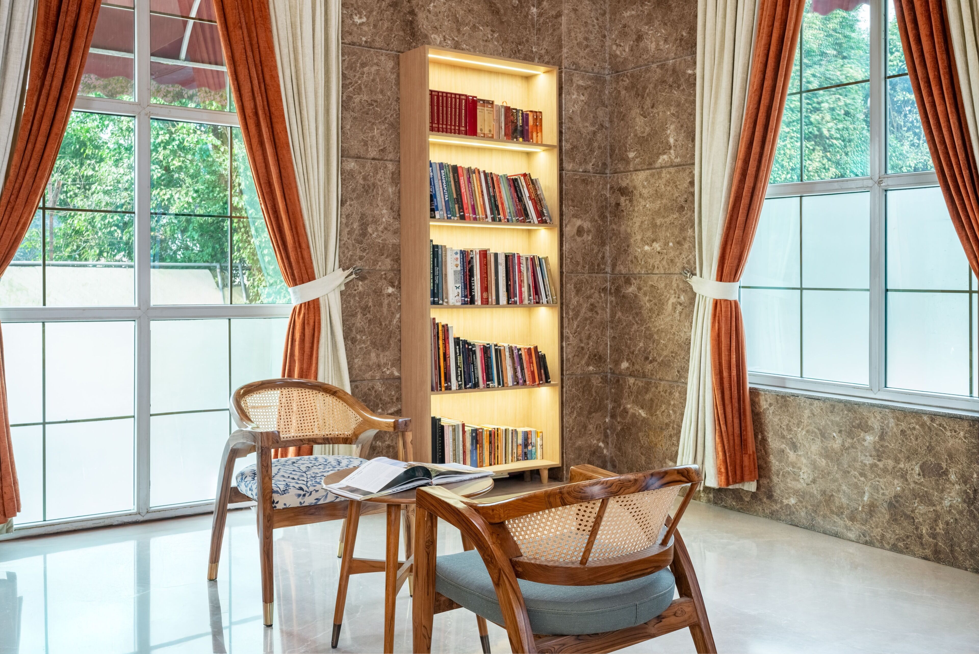 Une pièce avec une grande bibliothèque, deux fauteuils en osier et une table sur laquelle sont posés des livres.