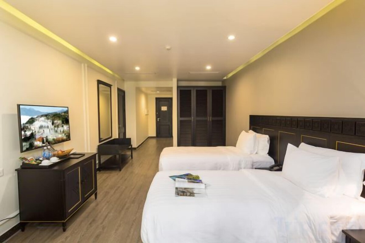 A hotel room with two beds, a TV, a desk, and a mirror.