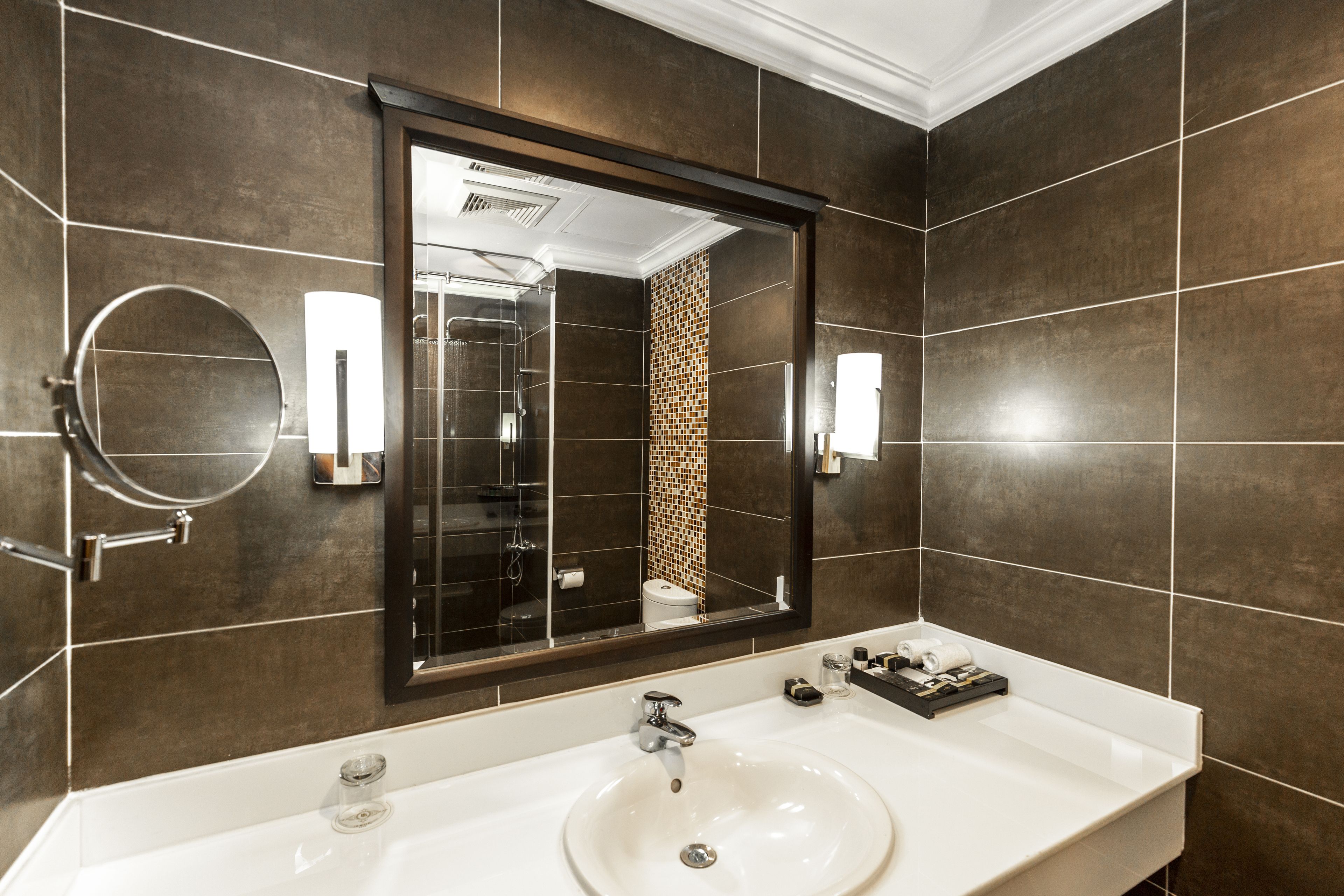 Un baño moderno con un espejo grande, un lavamanos blanco y una zona de ducha.
