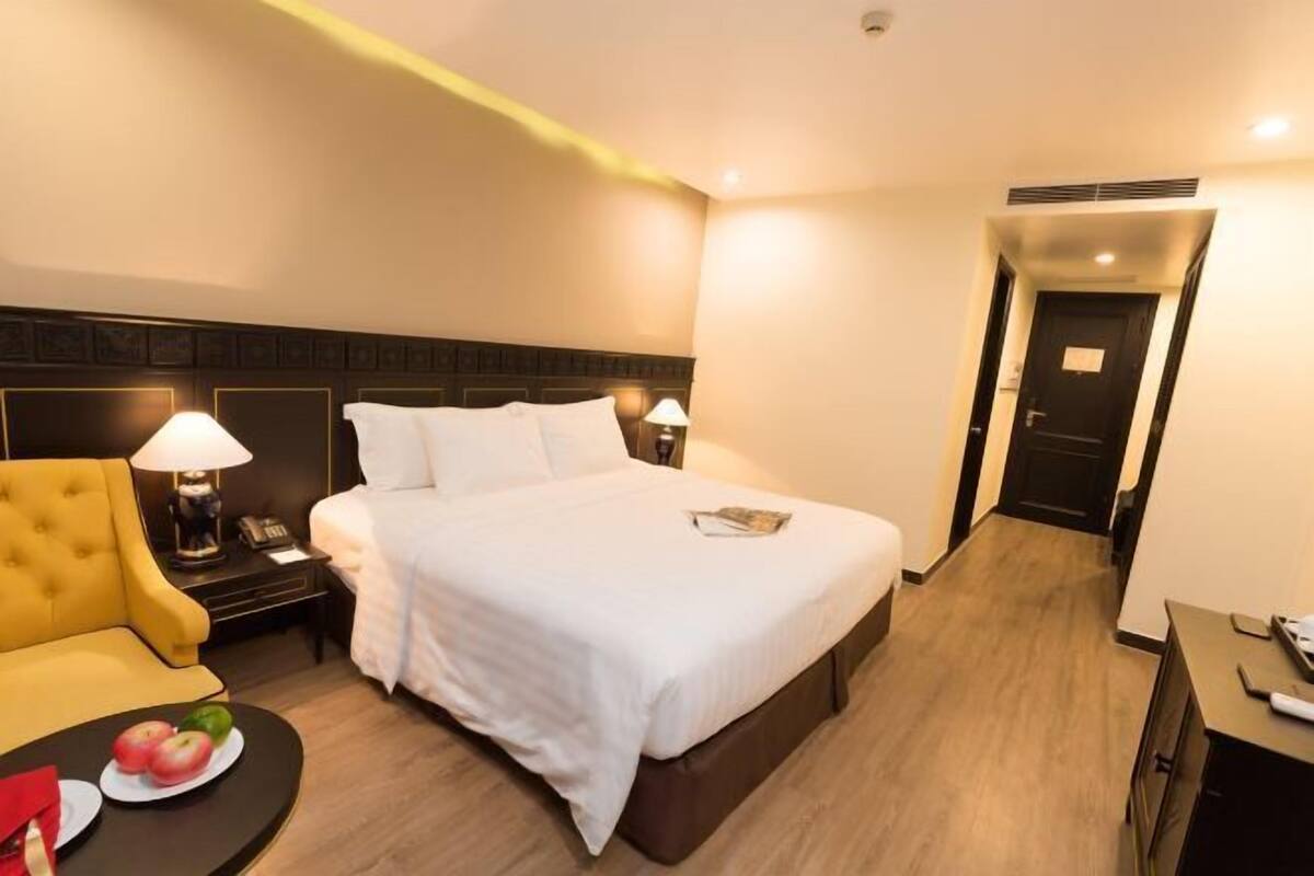 A hotel room with a bed, bedside tables, a sofa, and a small table with fruit.
