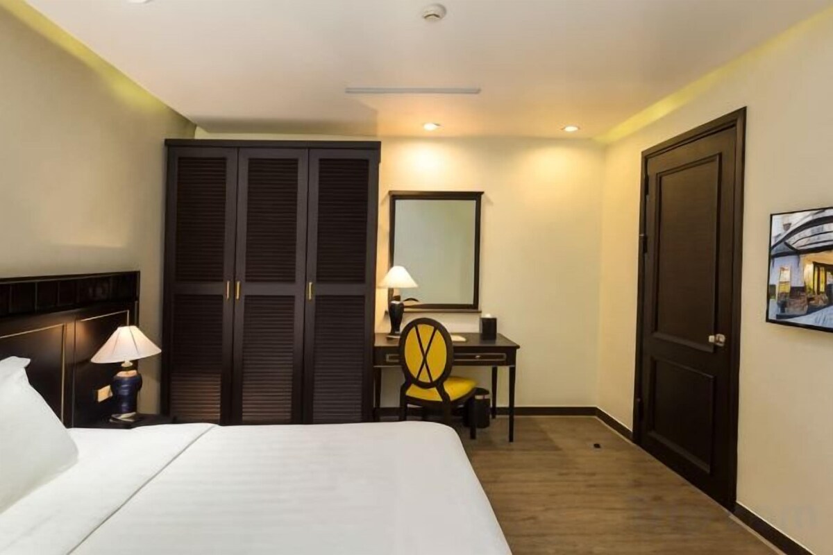 A hotel room with a bed, a desk with a chair, a wardrobe, and a door.