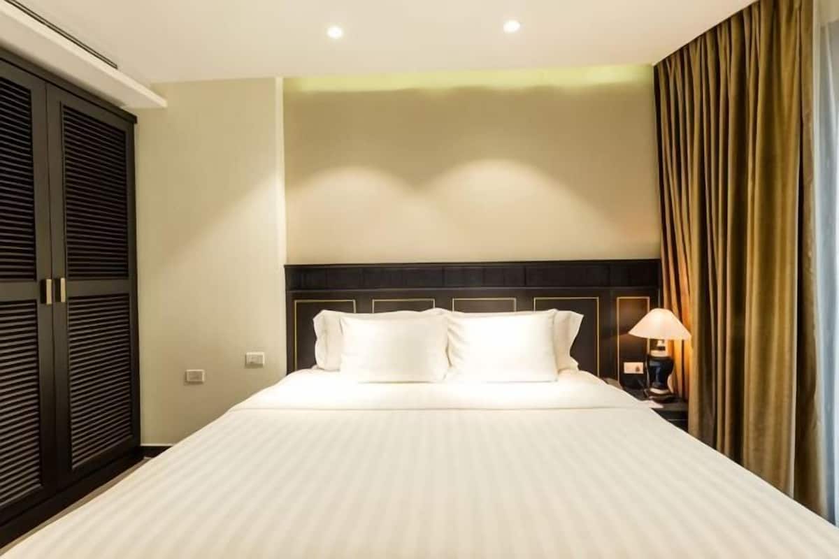 A hotel room with a large bed, a nightstand with a lamp, and a wardrobe.