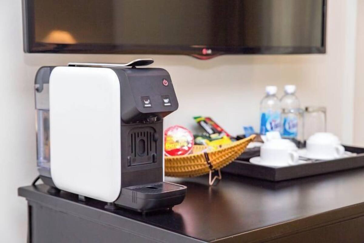 Une machine à café est posée sur un comptoir, à côté d’une pile de tasses, de bouteilles d’eau et d’un panier rempli de collations.