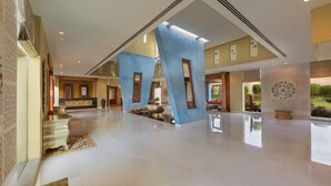 Un hall d’entrée spacieux avec un plafond haut, une fontaine centrale et une vue sur un jardin aménagé.