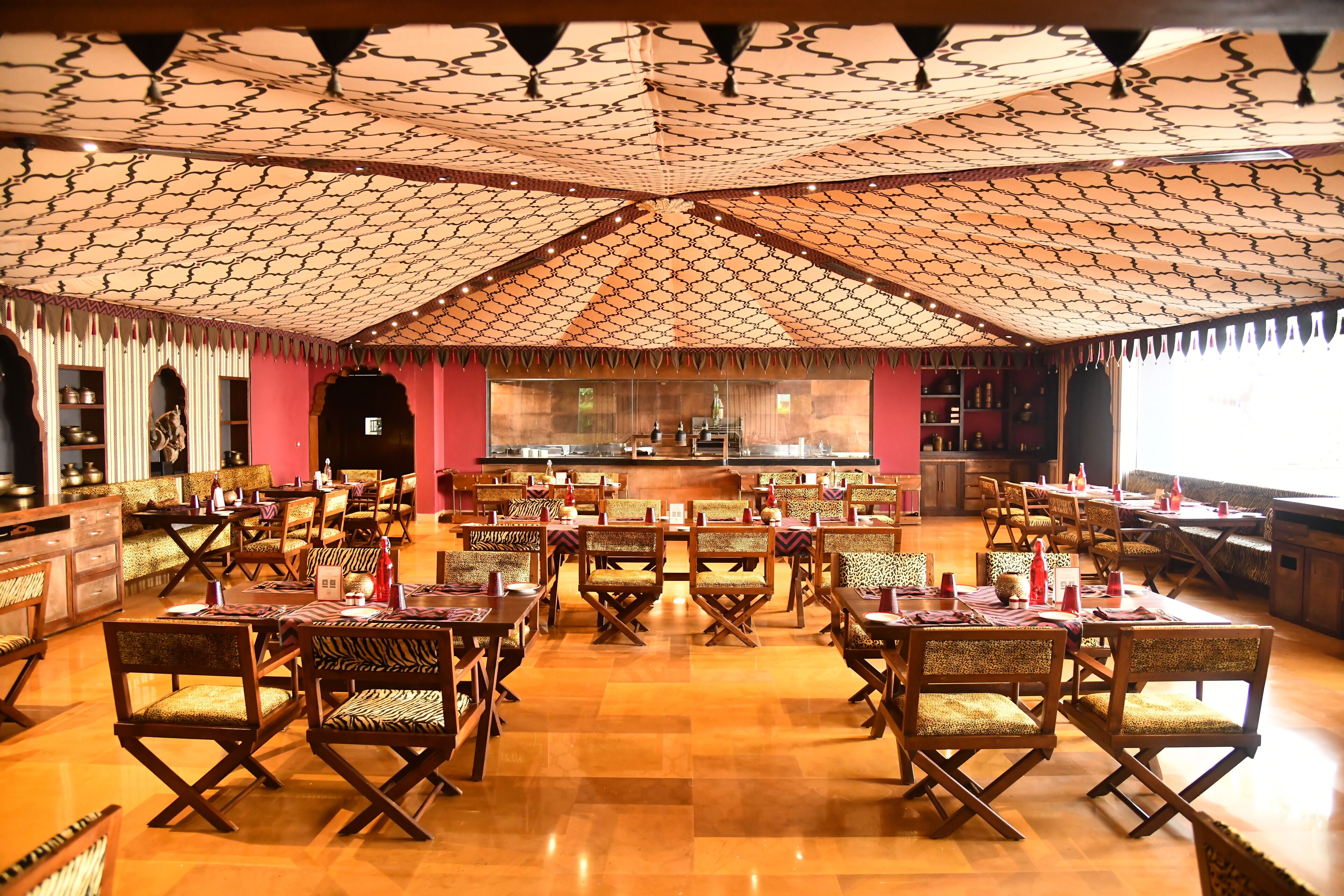 A restaurant with a high ceiling and patterned ceiling design, wooden tables and chairs, and a bar area in the background.