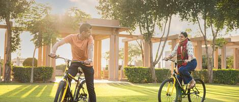 Two people riding bicycles in a park with a gazebo and trees.