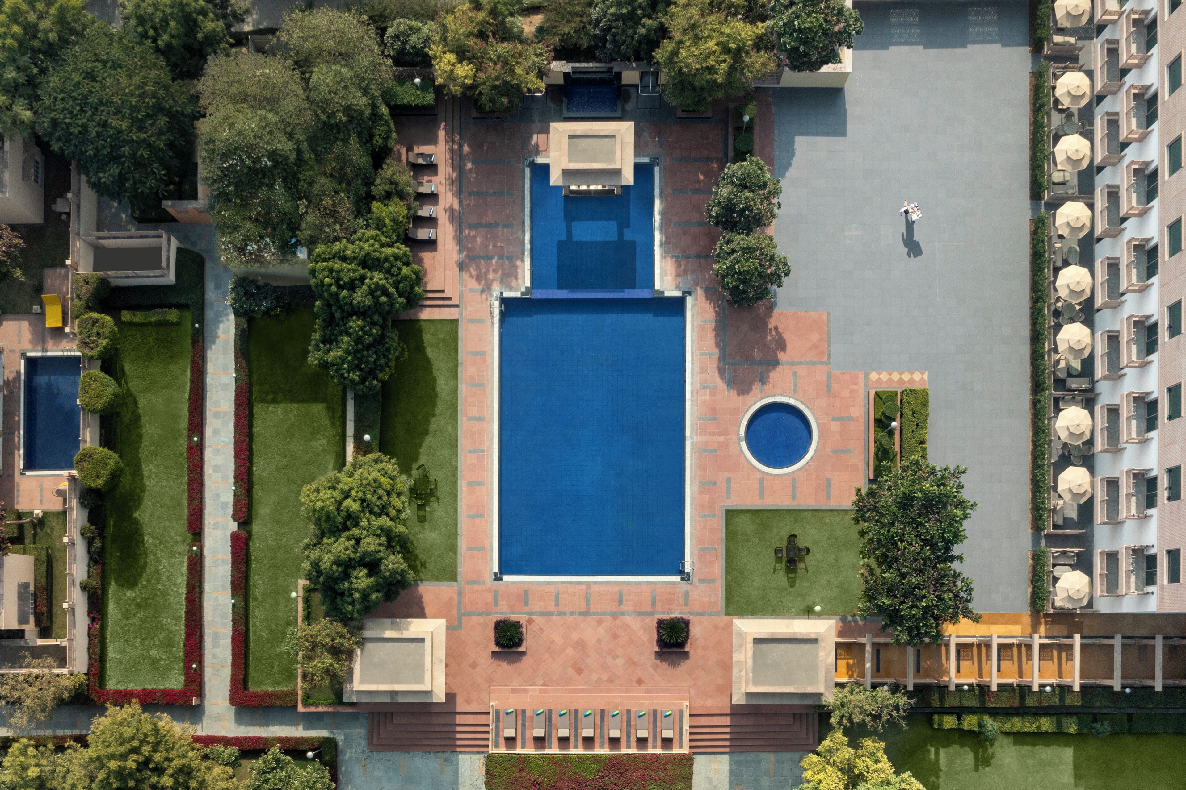 An aerial view of a residential building with a central swimming pool, surrounded by well-maintained gardens and a small circular water feature.