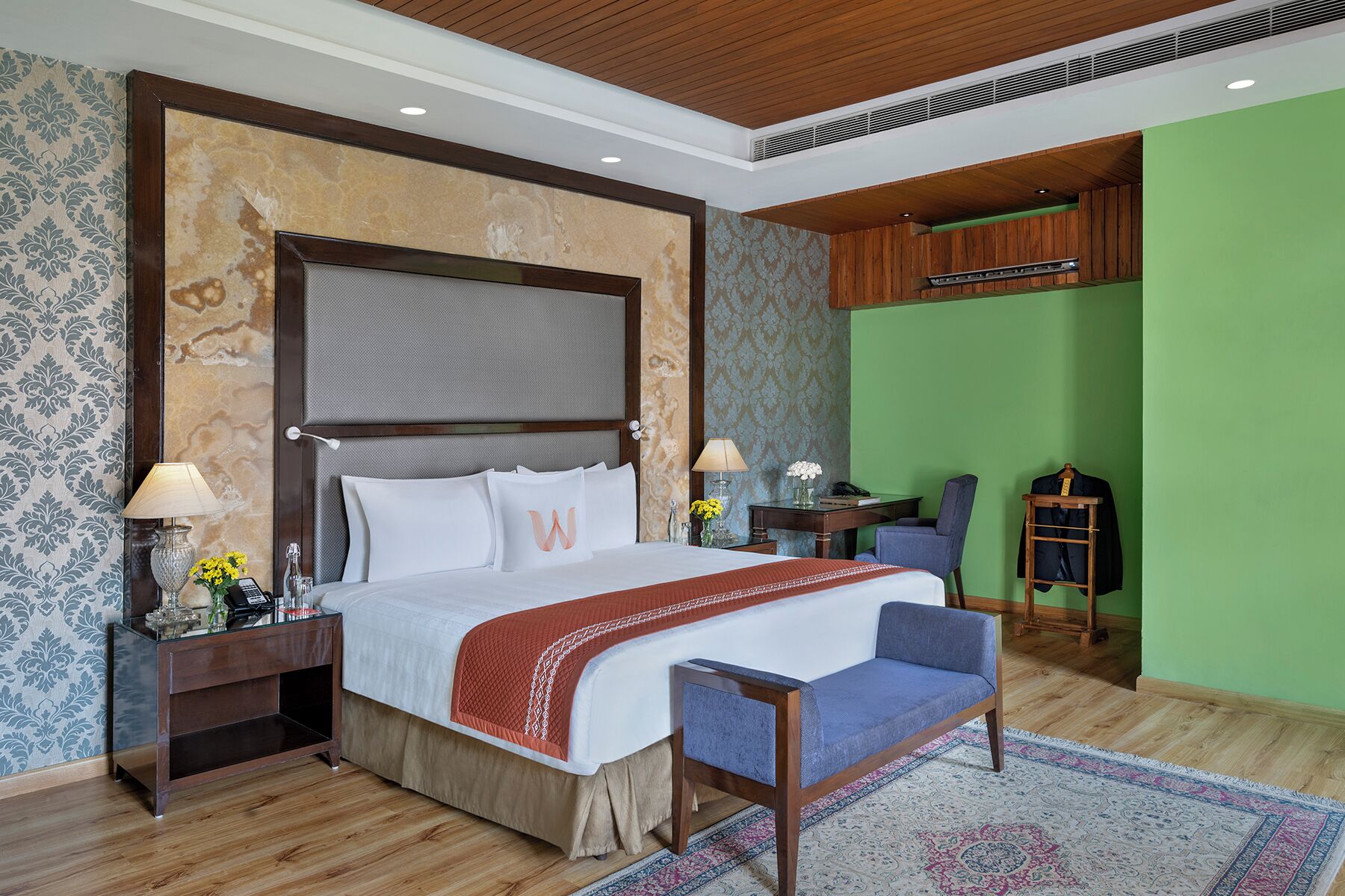 A hotel room with a large bed, a desk, a chair, a wardrobe, and a green accent wall.