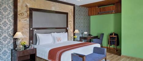 A hotel room with a large bed, a desk, a chair, a wardrobe, and a green accent wall.