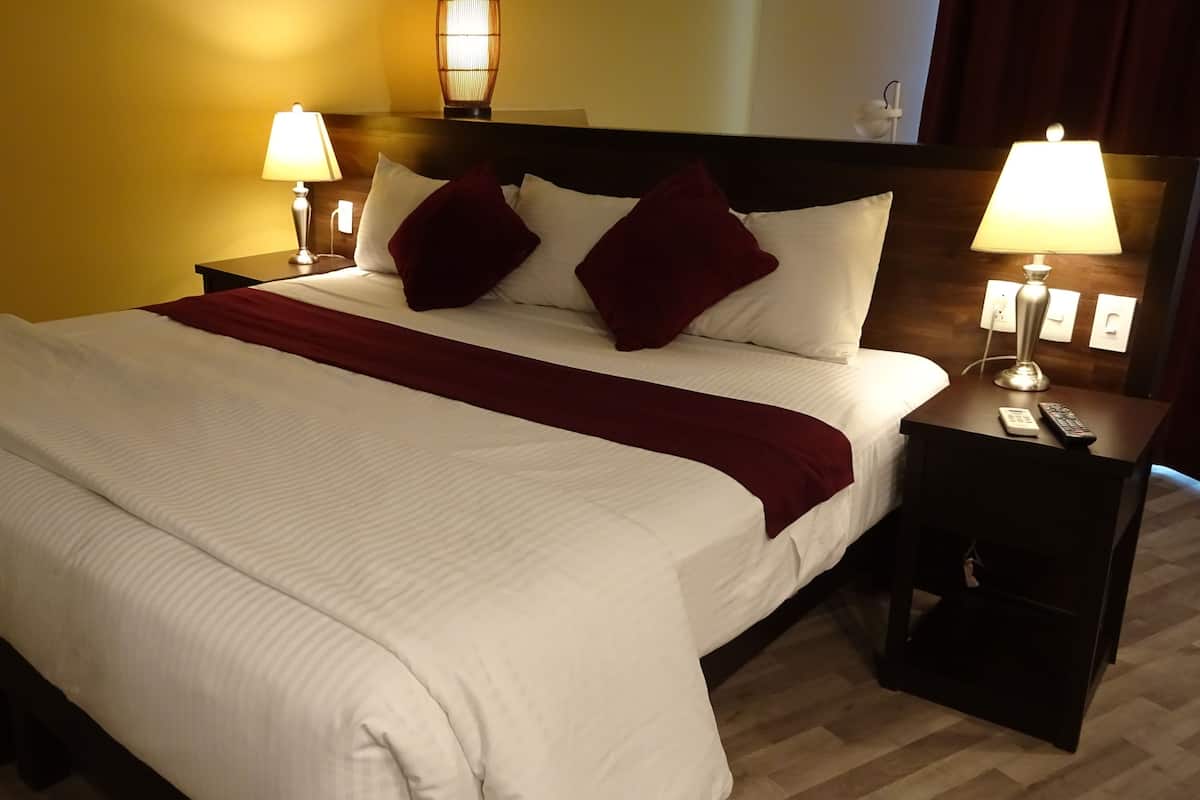 A hotel room with a large bed, two bedside lamps, a wooden headboard, and a red throw blanket.