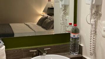 Una habitación de hotel con cama, un baño con lavamanos y una botella de agua sobre la encimera.
