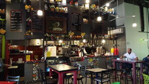 Interior de restaurante com várias mesas e cadeiras, um balcão com menu e girassóis decorativos.