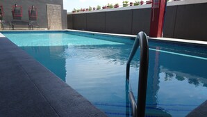 Uma piscina com superfície de água azul cristalina, escada de metal e borda revestida de azulejos.