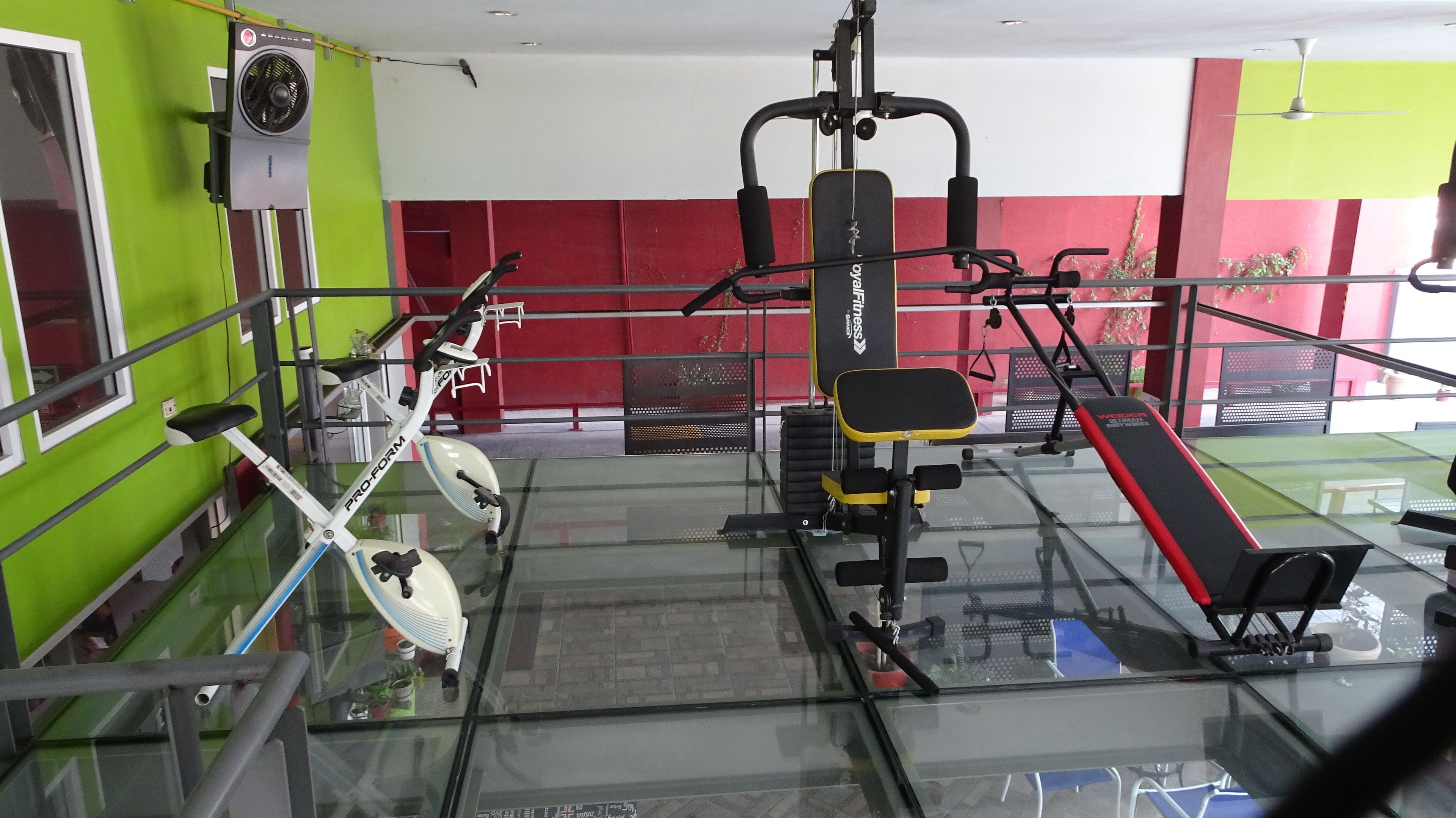 A gym with exercise equipment, a bench, and a fan on the wall.