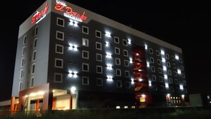 Um hotel de vários andares com sinalização iluminada, entrada destacada e padrões uniformes nas janelas.