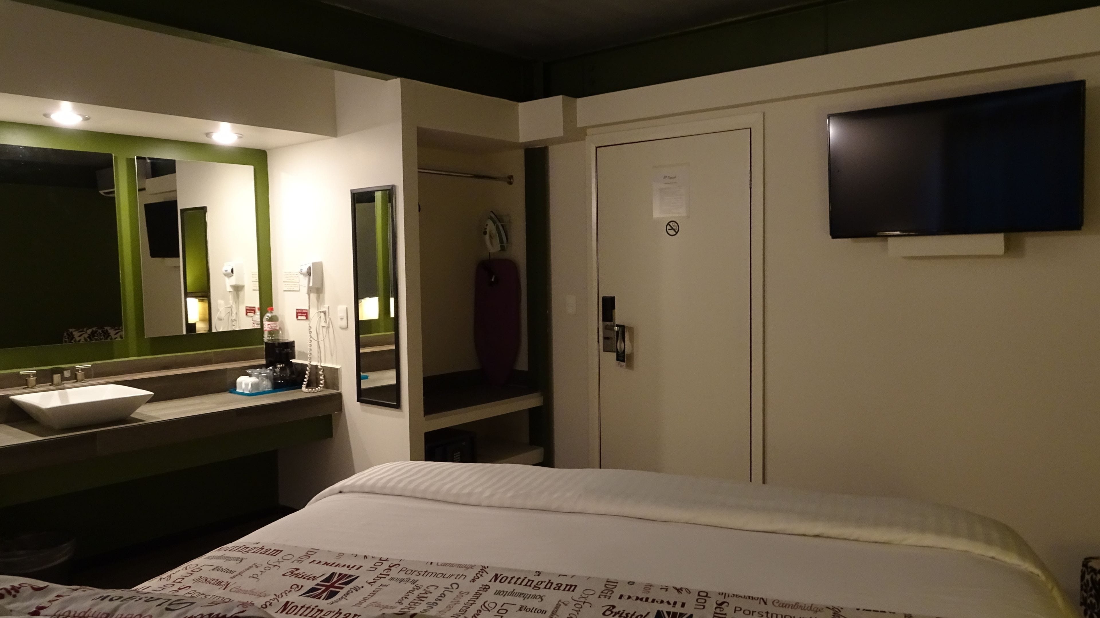 A hotel room with a bed, a large mirror, a sink, and a television.