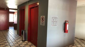 Un couloir avec des carreaux de sol à motifs, des portes rouges, un extincteur et une signalisation d’urgence.