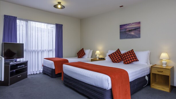 A hotel room with two beds, a TV, a painting, and a lamp. - Deans Bush Motel (Christchurch)