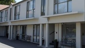 A modern hotel with multiple floors, large windows, and a covered outdoor seating area. - Deans Bush Motel (Christchurch)
