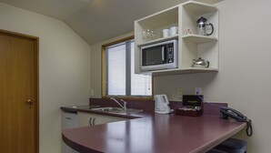 A compact kitchen with a microwave, kettle, and coffee maker on the counter, a sink, and a telephone. - Deans Bush Motel (Christchurch)