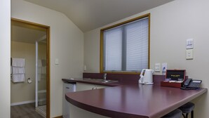 A compact kitchen with a built-in island, a window with blinds, and a telephone on the counter. - Deans Bush Motel (Christchurch)