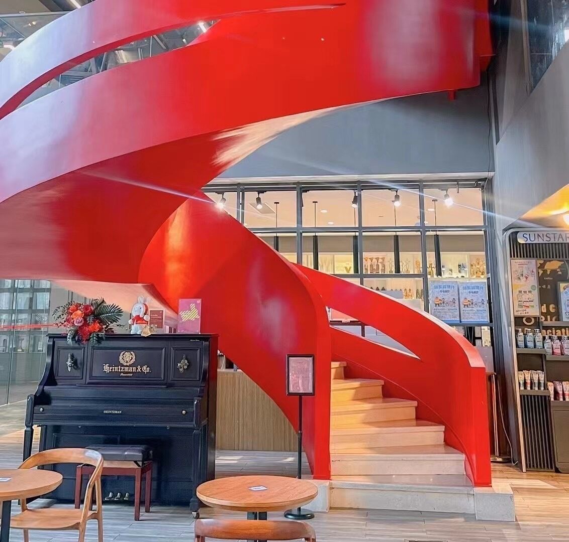 A modern interior with a red spiral structure, a black piano, and wooden tables.