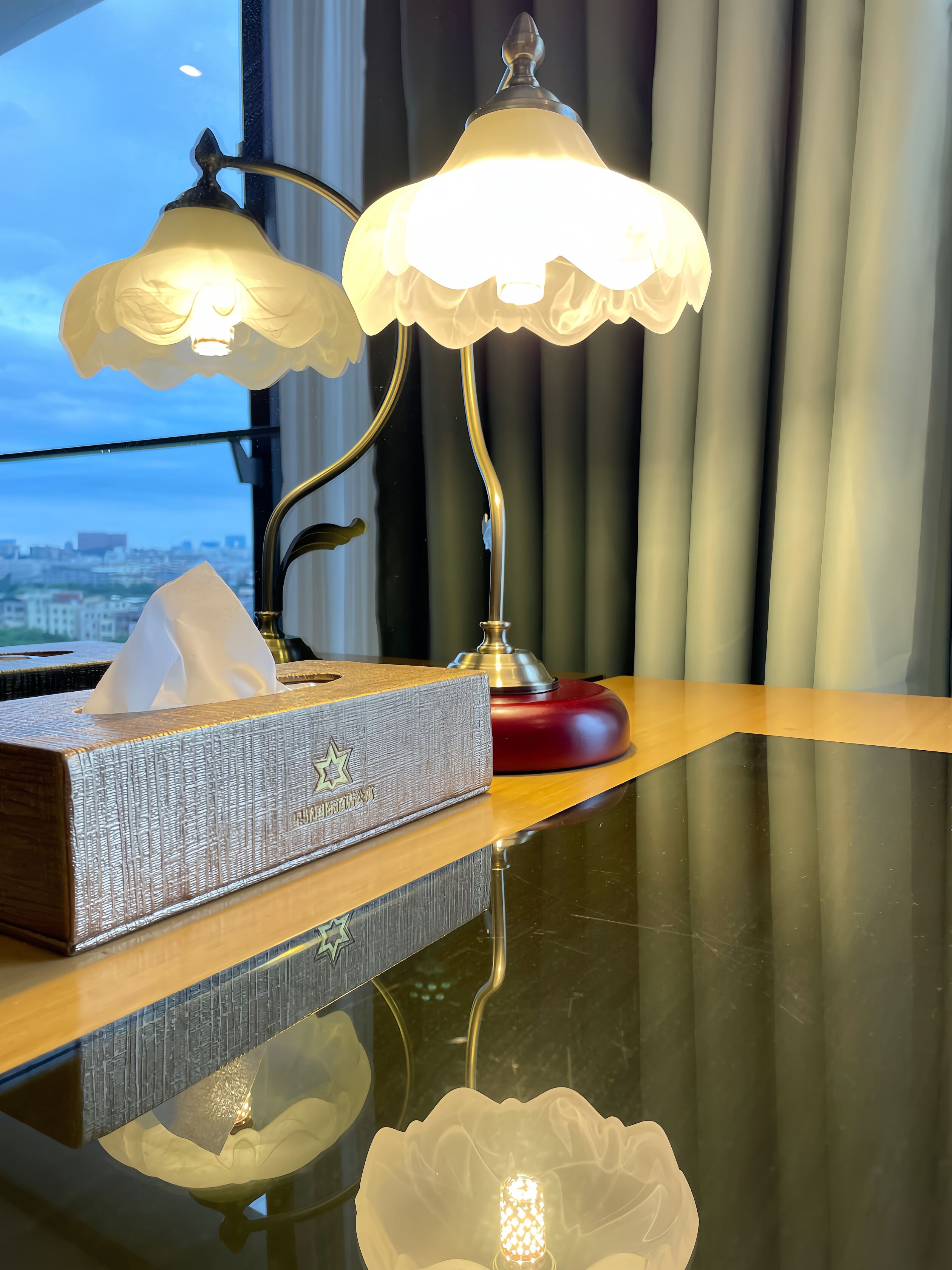 A hotel room with a desk featuring a tissue box and a lamp.