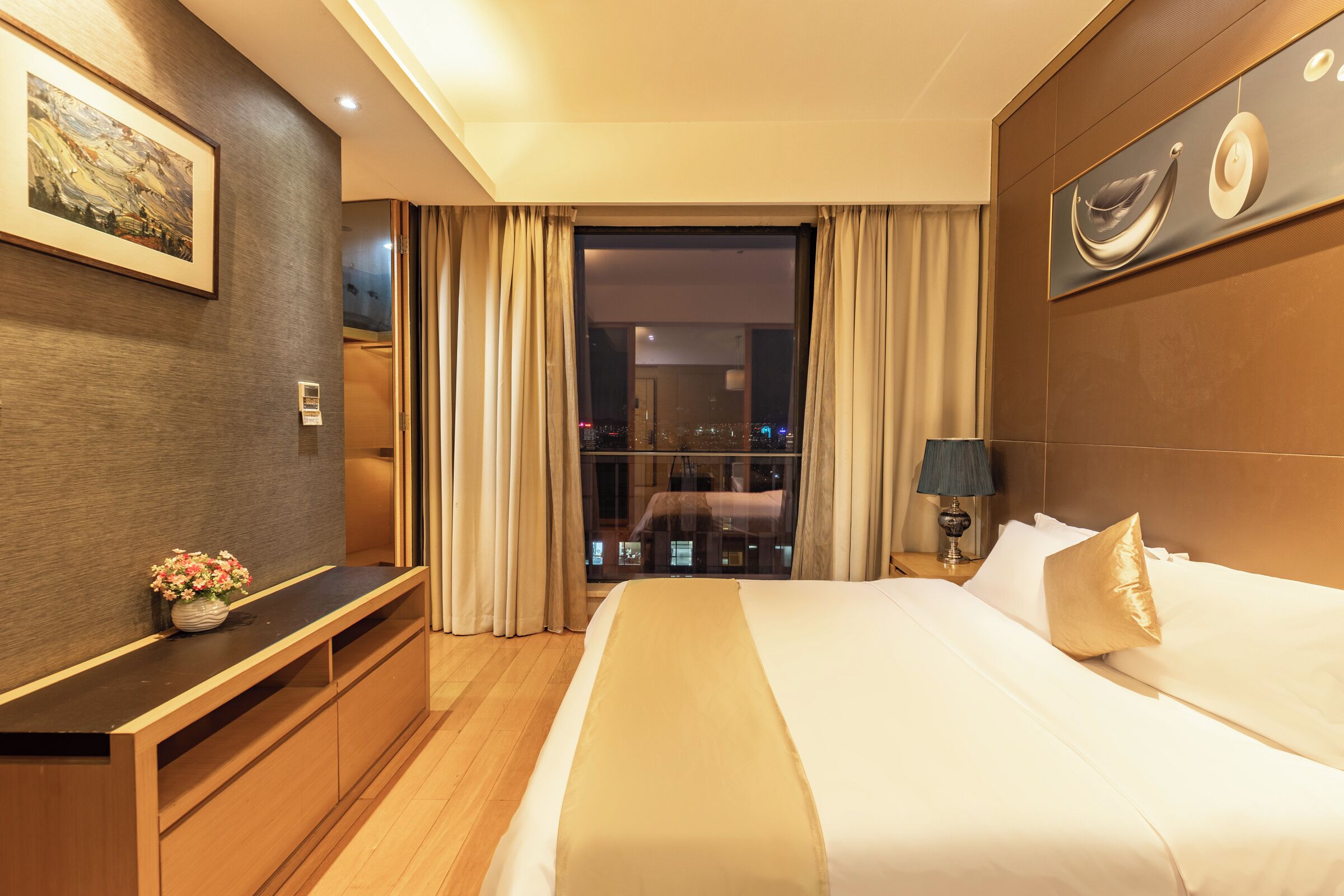 A hotel room with a large bed, a desk, a chair, a window with curtains, and a painting on the wall.