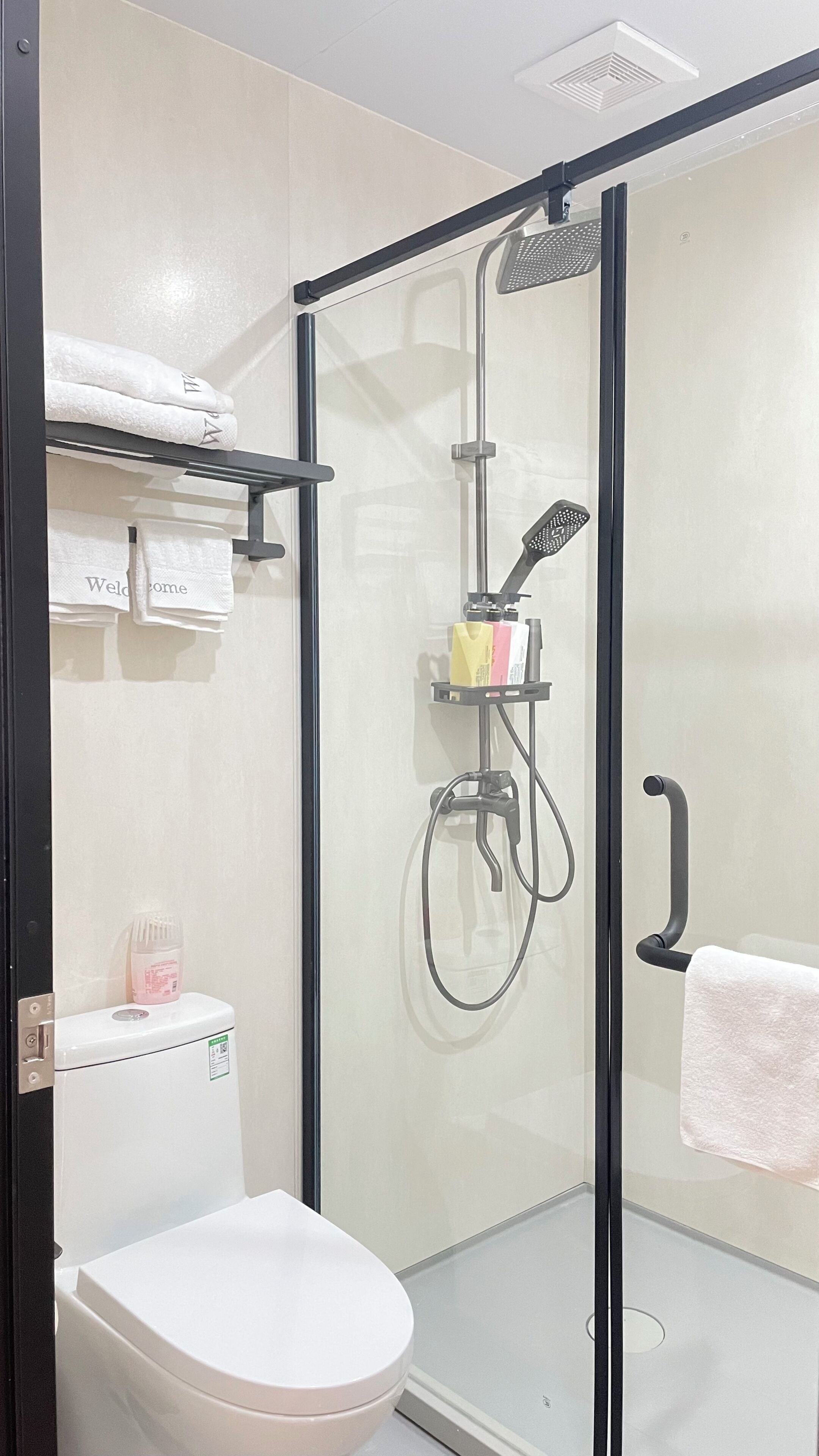 A modern bathroom with a glass-enclosed shower, a toilet, and a towel rack with folded towels.