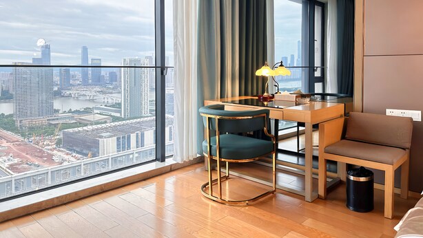 A modern hotel room with a large window, a desk, a chair, and a lamp. - Xingyi International Hotel Poly Store (Guangzhou)