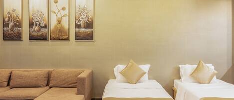 A hotel room with a sofa, two beds with gold accents, and three framed floral paintings on the wall.