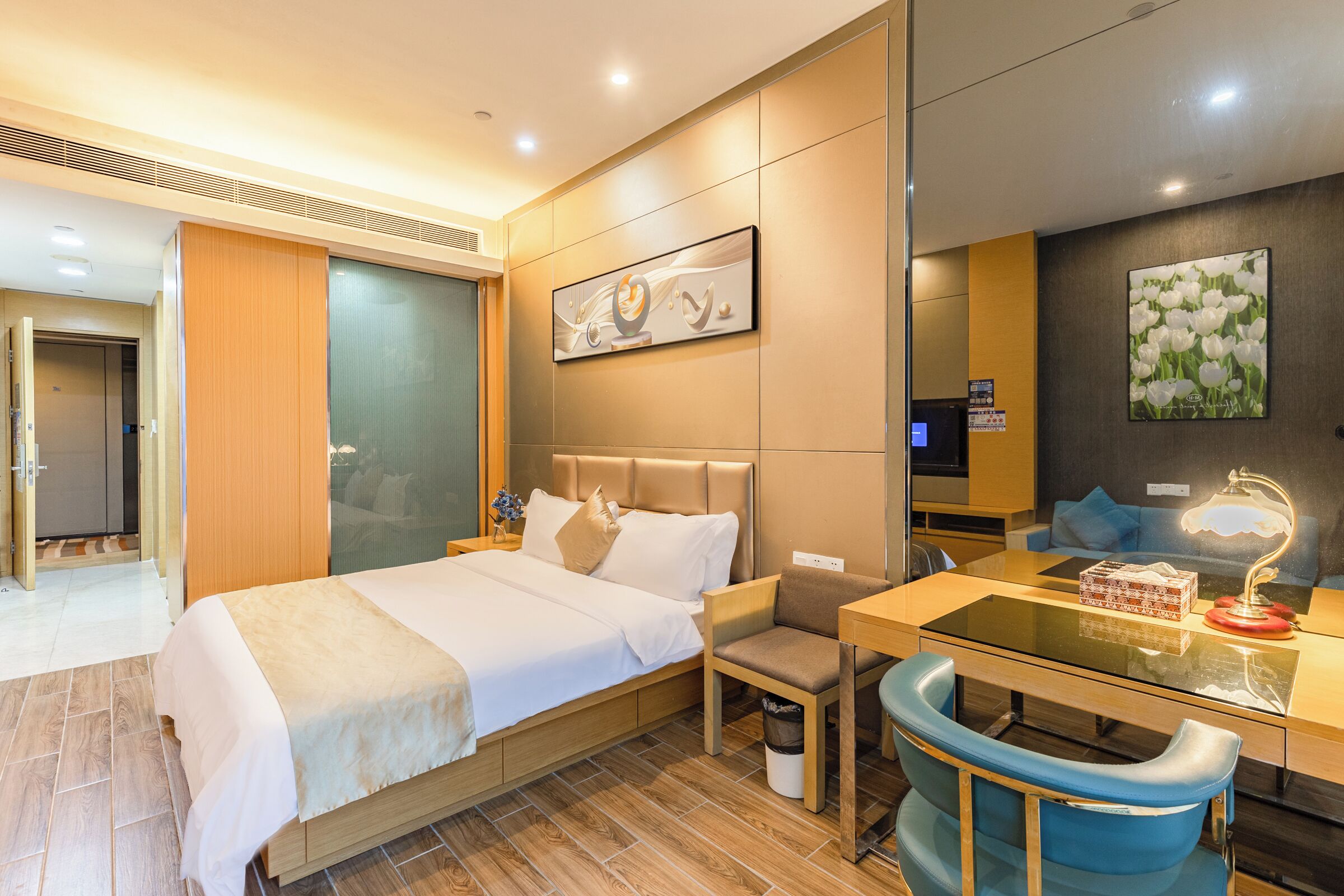 A modern hotel room with a bed, desk, chair, and artwork on the walls.