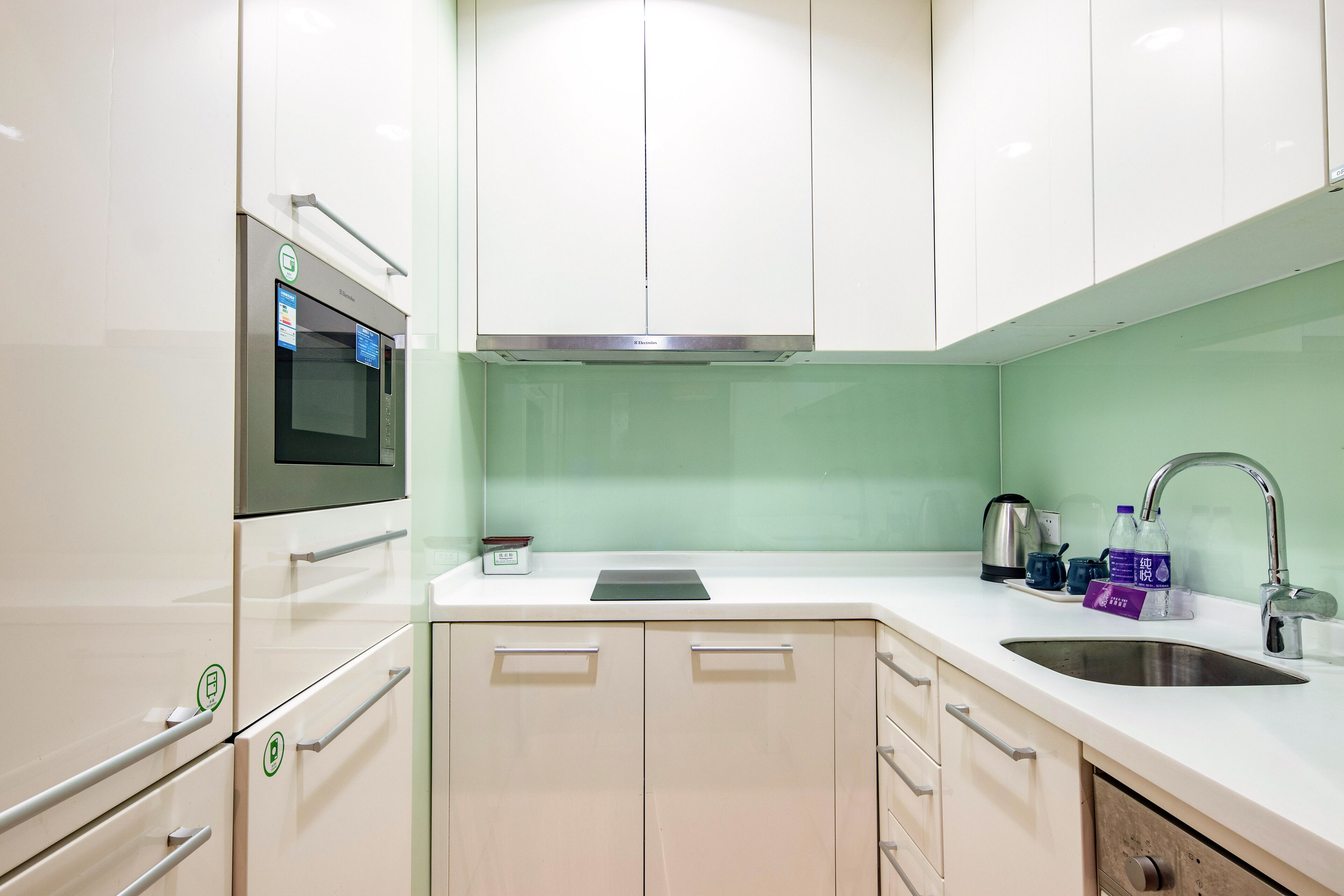 Una cocina moderna con armarios blancos, horno de acero inoxidable, microondas integrado, pileta de acero inoxidable y salpicadero verde.