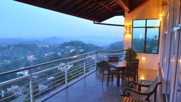 A balcony with a table and chairs, a railing, and a view of a town and mountains. - Amaara Sky Hotel (Kandy)