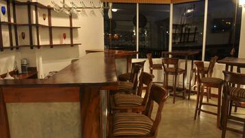 Un restaurante con barra de madera, sillas con cojines a rayas y vista de la ciudad de noche.
