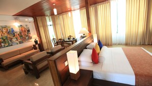 A hotel room with a bed, a sofa, a desk, and a painting on the wall. - Amaara Sky Hotel (Kandy)