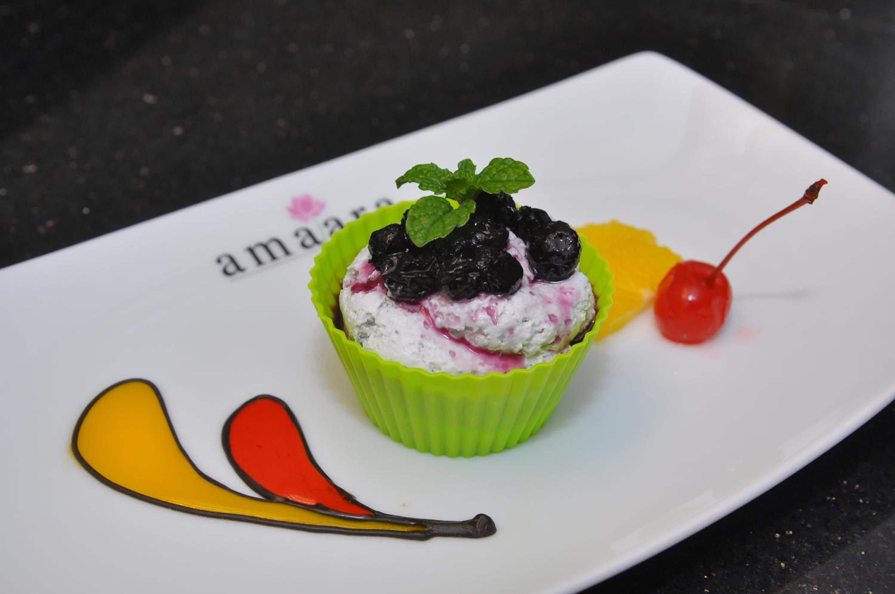 A dessert in a green cup on a white plate with a black background.