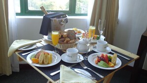 A breakfast table with plates of fruit, bread, and juice, set on a mat near a window. - Amaara Sky Hotel (Kandy)
