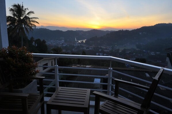 A balcony with a view of a sunset over a cityscape, including a waterfall and palm trees.