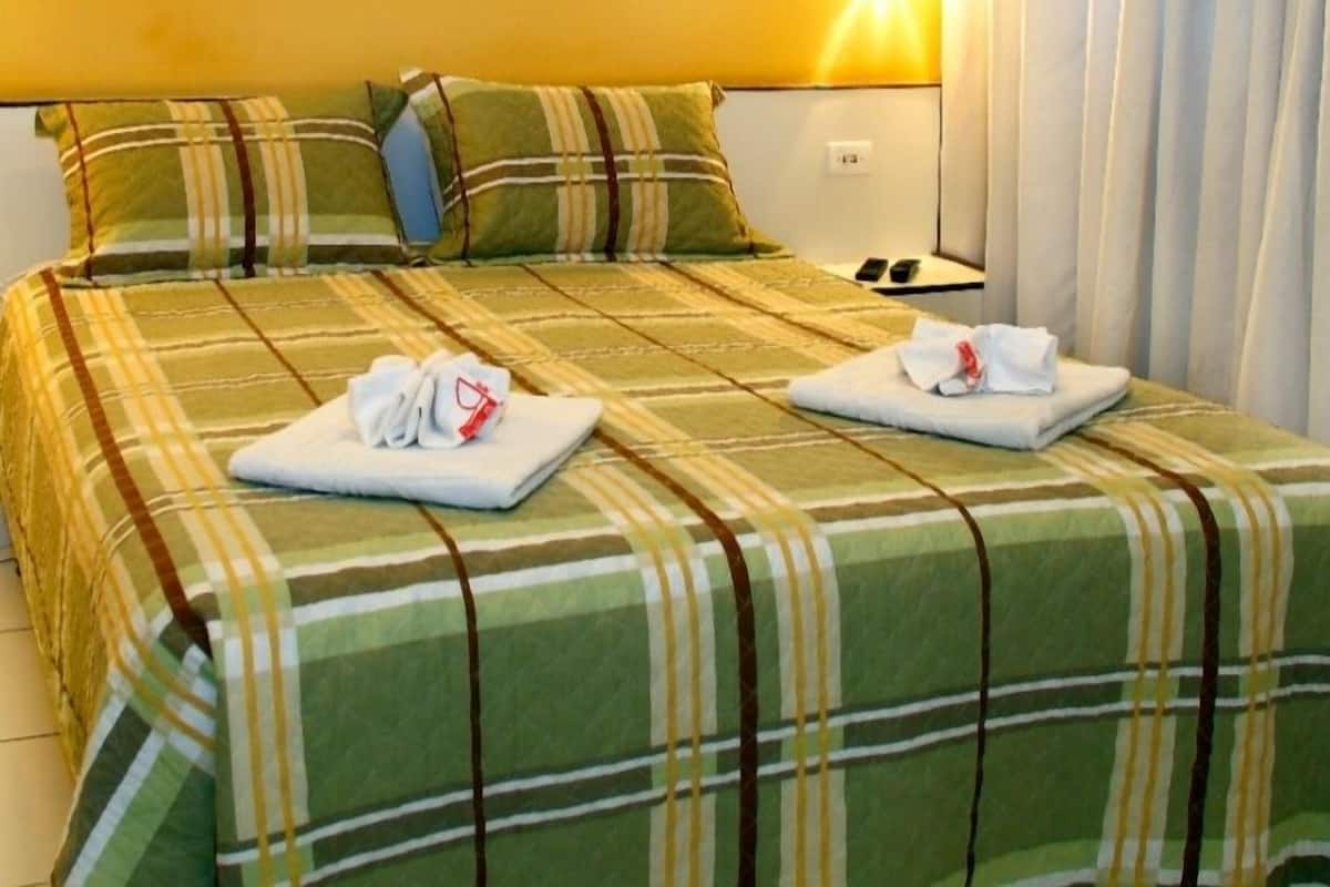 Ein Hotelzimmer mit Bett, Kissen, einem Bild an der Wand und einem Nachttisch mit Lampe.